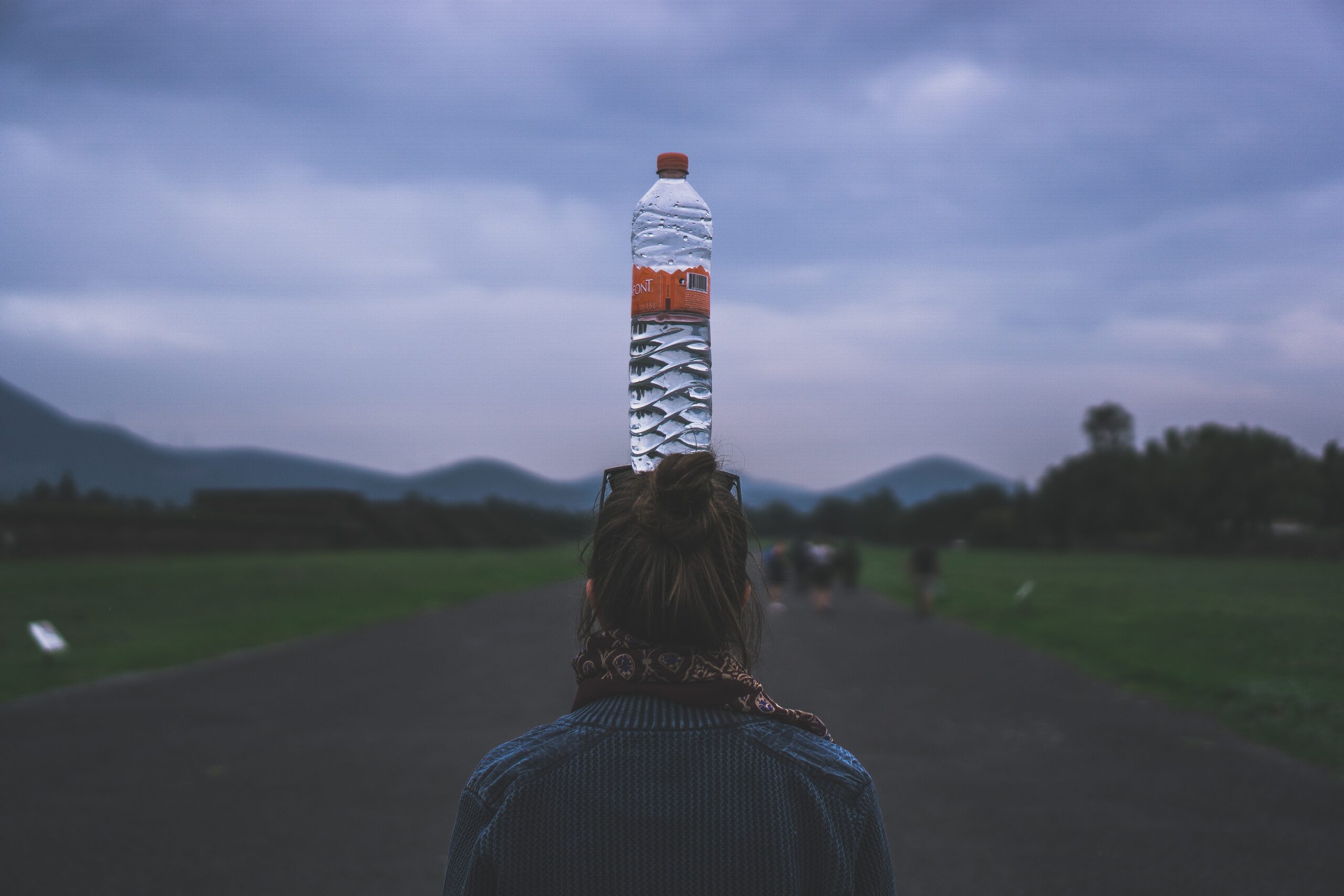 Bilde av kvinne bakfra med vannflaske på hodet.