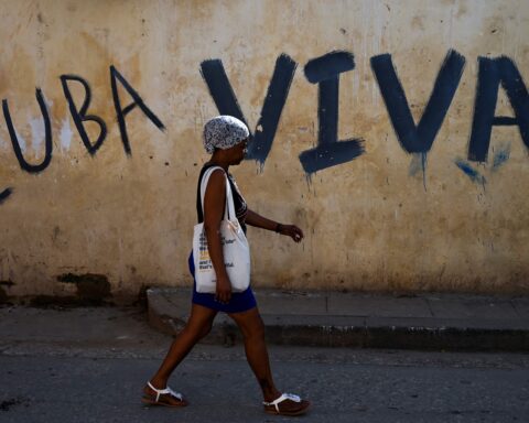 Bilde av en kvinne i en gate i Havanna hvor det er skrevet «Cuba viva», «Cuba lever», på en husvegg.