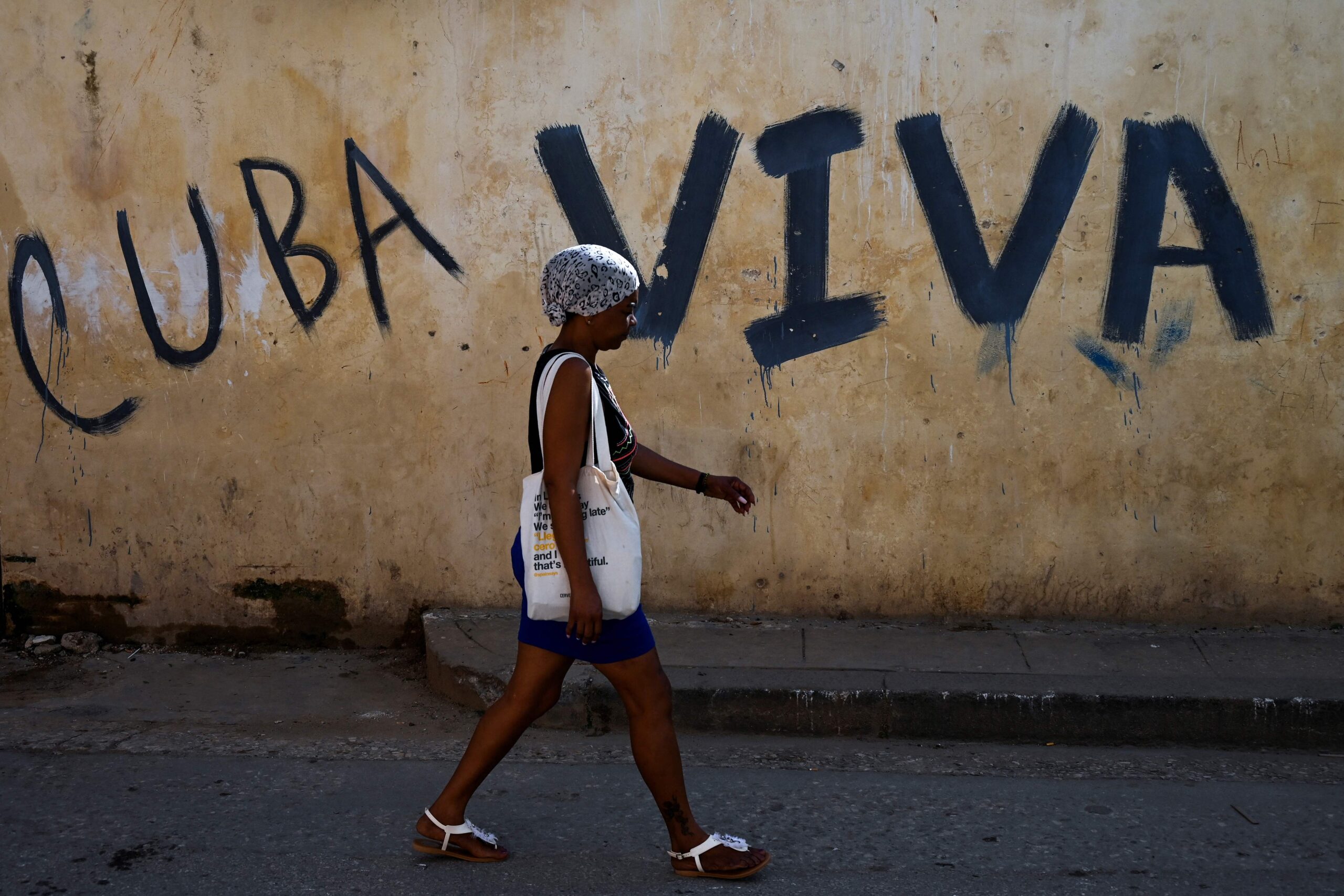 Bilde av en kvinne i en gate i Havanna hvor det er skrevet «Cuba viva», «Cuba lever», på en husvegg.